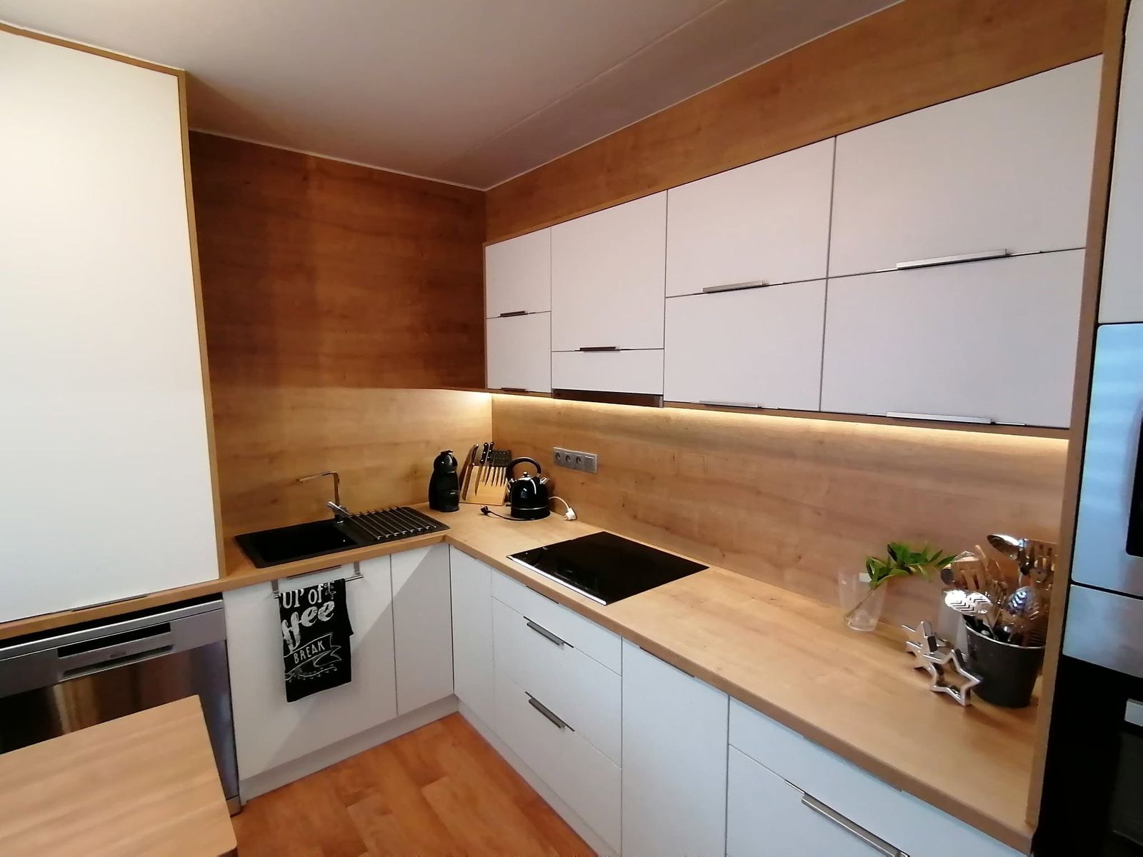 Bílá kuchyň s dřevěným obkladem a LED podsvícením